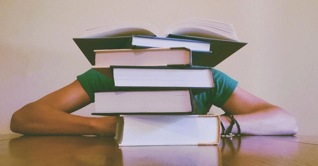 Person hiding behind a stack of books to represent education, one of the core values of Summit Birth