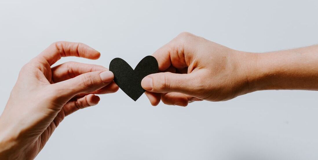 Two hands holding a black paper heart to represent support during the childbearing year